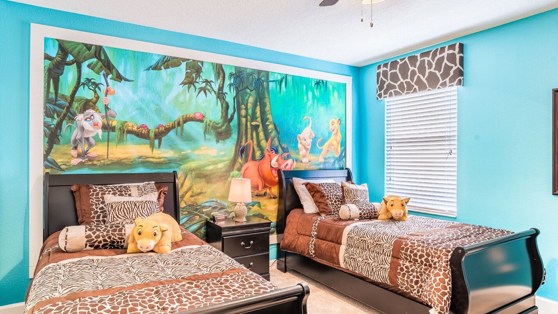 Een slaapkamer met twee bedden, elk met een beddeken met girafmotief, een grote jungle muurschildering en een giraf knuffel op een van de bedden.