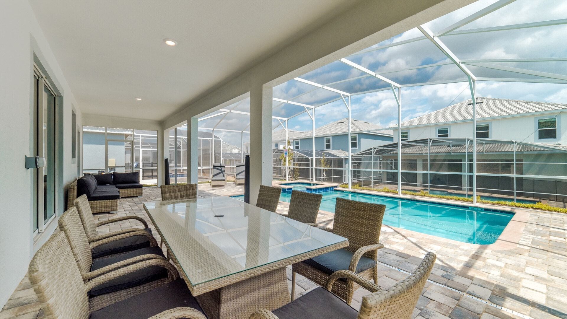 Un patio amplio con una mesa de vidrio y sillas de mimbre, con vistas a una piscina y una zona residencial.