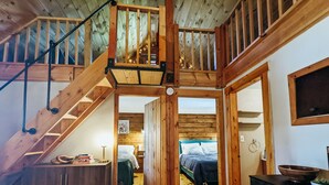 Un intérieur en bois avec un escalier menant à une mezzanine, un lit doté d’une tête de lit bleue et une armoire en bois.
