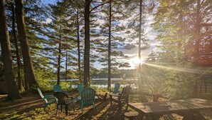 Un terrain de camping équipé de tables et de chaises pour pique-nique, entouré de grands arbres et offrant une vue sur un lac.