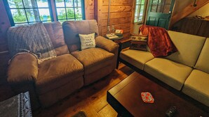 L’intérieur d’un chalet chaleureux, avec un canapé marron, un canapé blanc et un plancher en bois.