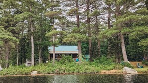 Une cabane entourée de grands arbres et bordée par un plan d’eau.