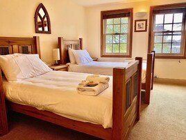 Una habitación con dos camas de madera, un espejo y dos ventanas que dan a zonas verdes.