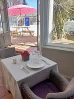 Un comedor con una mesa dispuesta para dos personas, vistas al exterior y un patio con una sombrilla roja.
