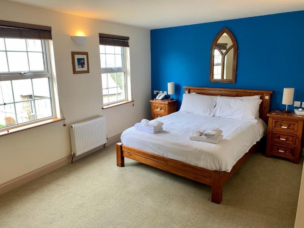 Een net opgemaakt bed met witte lakens en handdoeken, een houten hoofdbord en een blauwe accentmuur.