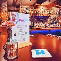 Pizarra de menú para 'Tennerville Fest' con opciones de almuerzo y cena, una zona de bar con botellas, y un cartel del hotel 'La Ville'.
