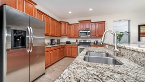 A modern kitchen with granite countertops, stainless steel appliances, wooden cabinets, and a built-in sink. - Last Minute Disney Getaway! Private Pool, Hot Tub & Game Room. Book Now! #38570 (Orlando)