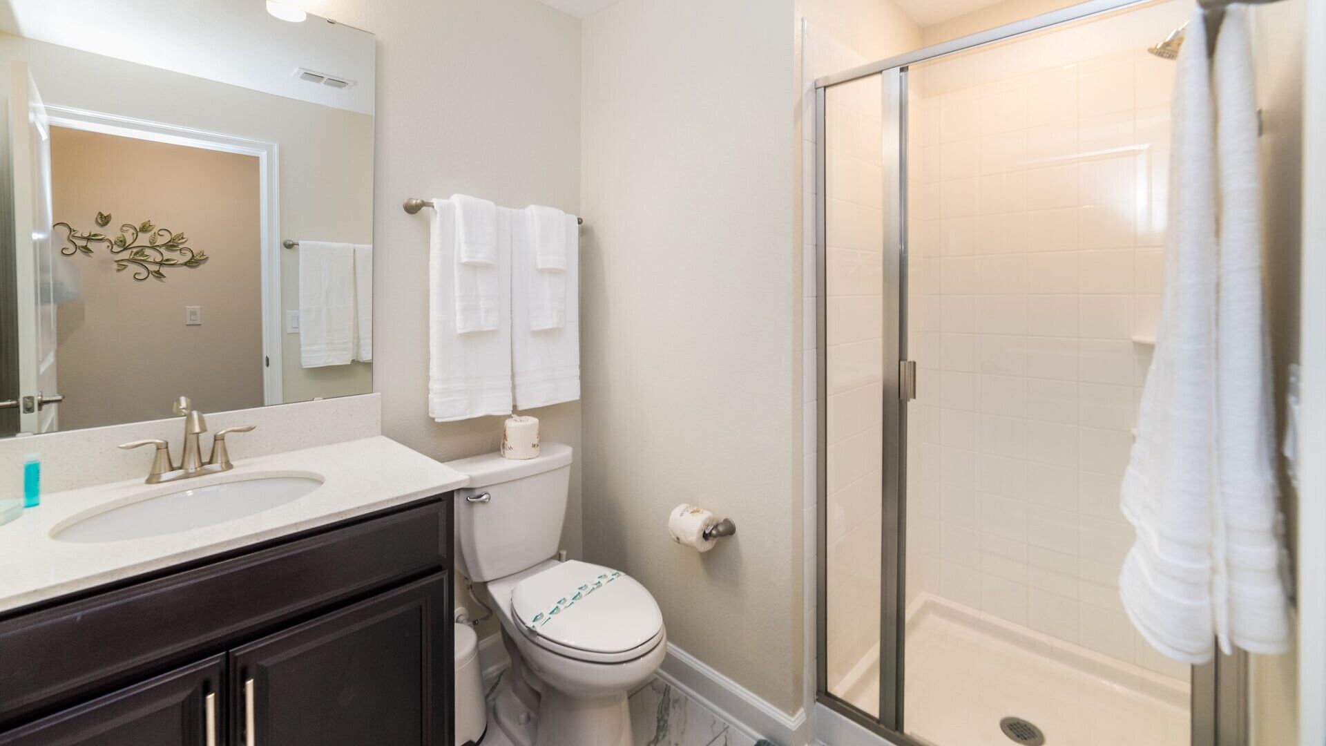 A modern bathroom with a white sink, a toilet, a glass shower enclosure, and a large mirror.