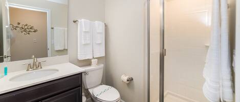 A modern bathroom with a white sink, a toilet, a glass shower enclosure, and a large mirror.