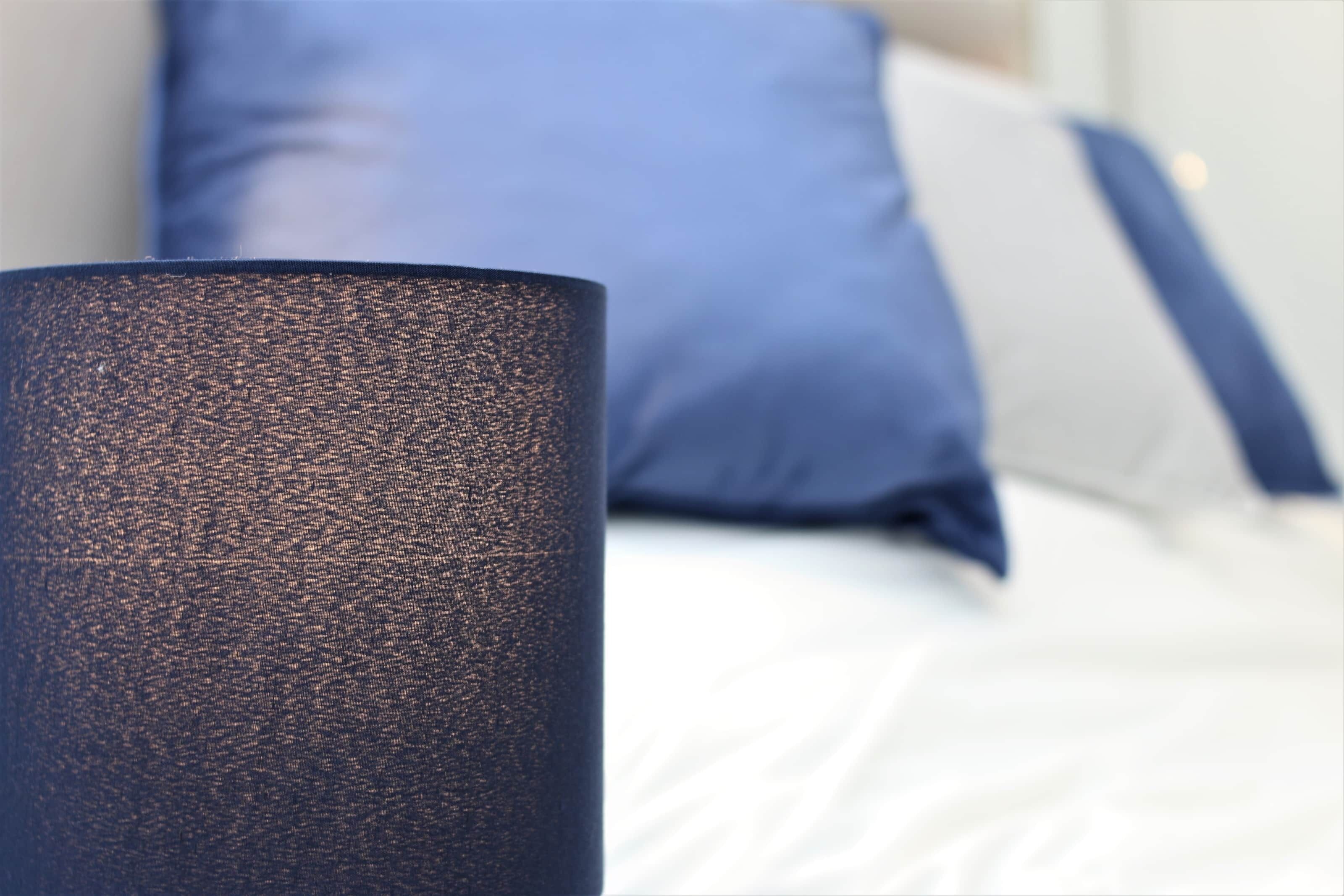 A close-up of a textured cylindrical object, possibly a lamp, in a room with a bed and pillows.