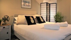 A neatly made bed with white linens and two black pillows with pineapple designs, a bedside fan, and a small plant on the nightstand. - Janet Street Loft (3 beds) (Cardiff)