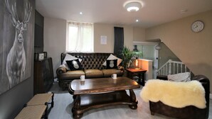 A living room with a leather sofa, a wooden coffee table, a fur throw, and a painting of a deer. - Janet Street Loft (3 beds) (Cardiff)
