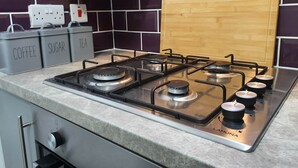 A kitchen with a gas stove, labeled containers for coffee, sugar, and tea, and a wooden cutting board.