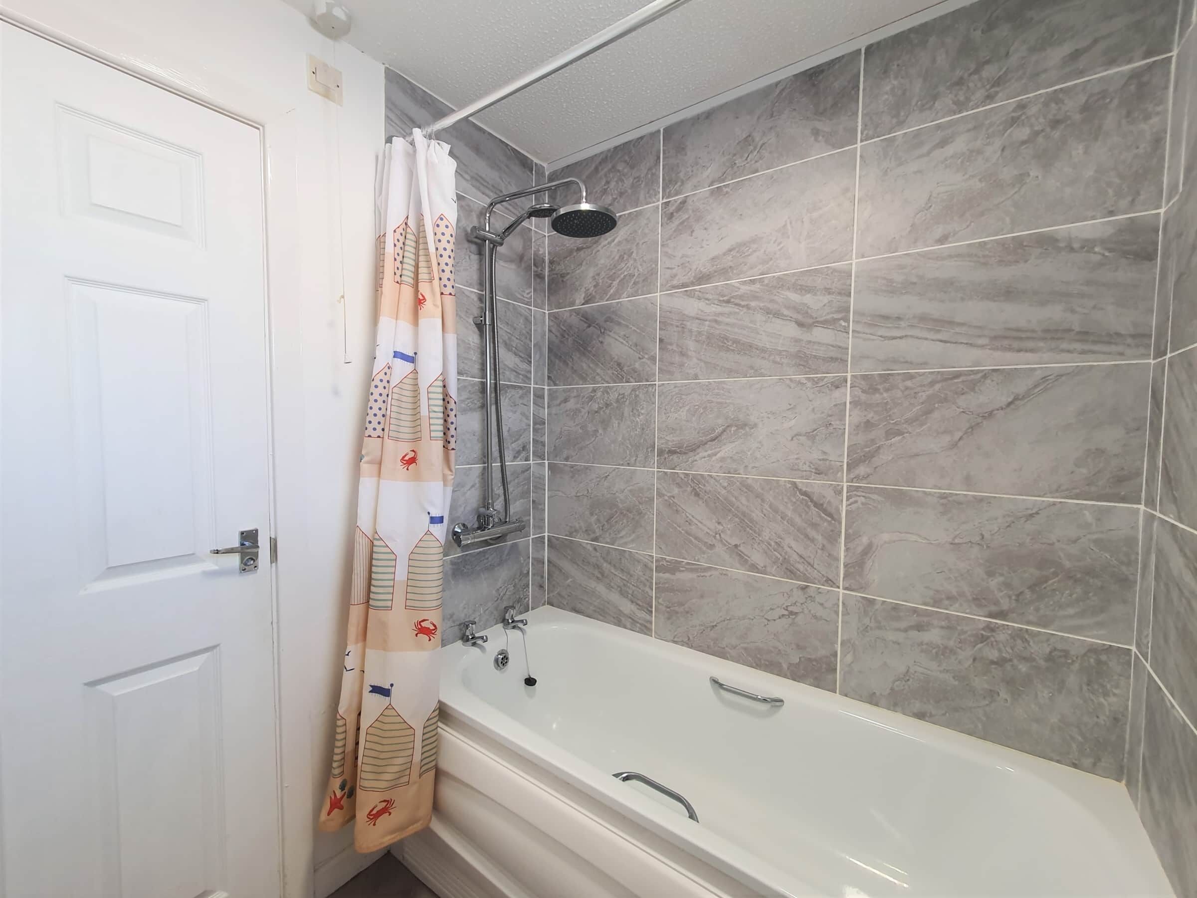 Ein Badezimmer mit einer Badewanne, Dusche und grauen Marmorfliesen.