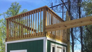Una casita de juegos de madera con un tobogán, una puerta y un cartel con las normas del parque infantil.