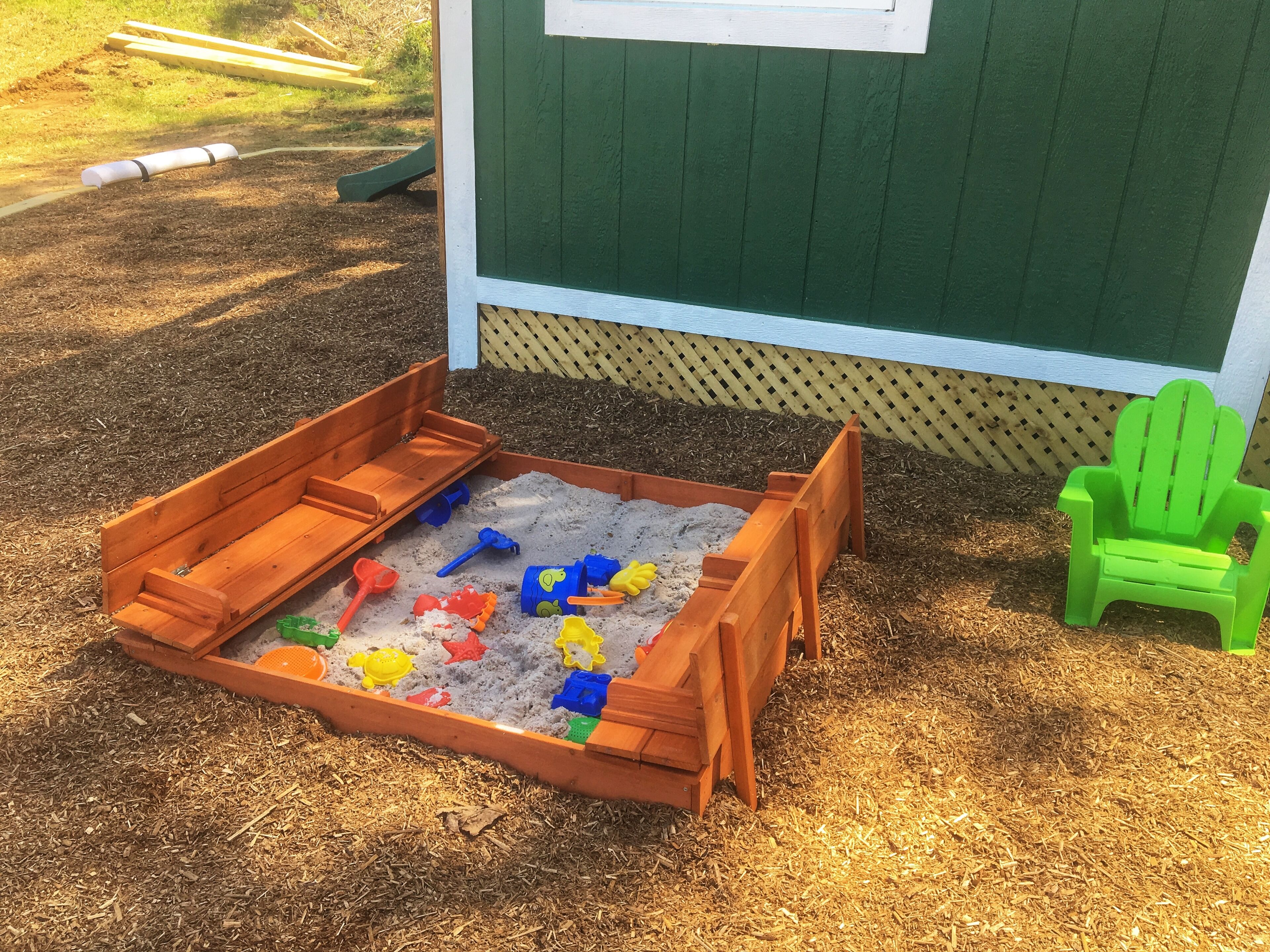 A sandbox with toys and a green chair.
