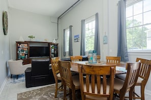 Uma sala de jantar com mesa e cadeiras de madeira, televisão e estante de livros.