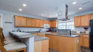 A modern kitchen with wooden cabinets, a central island, a microwave, and a clock on the wall.