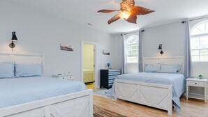 A bedroom with two white beds, a ceiling fan, and a window with curtains.