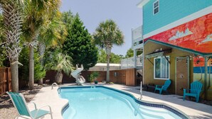 A backyard with a swimming pool, a slide, and a deck with chairs.
