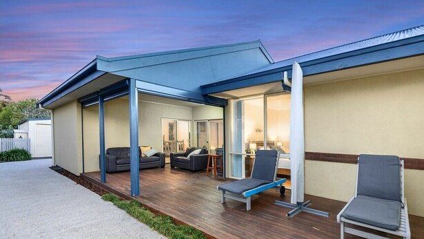 A modern house with a covered patio, a living room with a sofa and chairs, and a visible kitchen area.