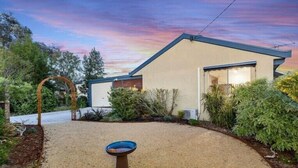 A modern house with a well-maintained garden, a bird bath, and a clear view of the sky.