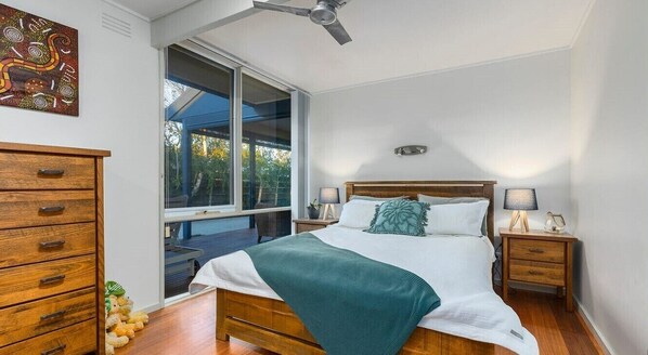A bedroom with a bed, wooden nightstands, a ceiling fan, a window, and a dresser. - Spacious 3 bedroom family holiday house (sleeps 8) (Tootgarook)