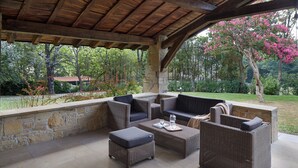 An outdoor patio with wicker furniture, stone walls, and a view of a garden with trees and flowers. - Villa Jaizubia Golf by FeelFree Rentals (Hondarribia)
