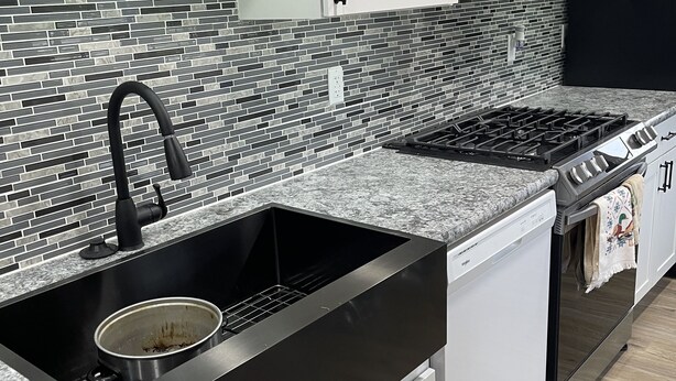 Una cocina moderna con un lavamanos negro, estufa de acero inoxidable y armarios blancos.