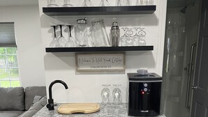 Cocina compacta con lavavajillas integrado, cafetera y un espacio para copas de vino sobre la encimera.