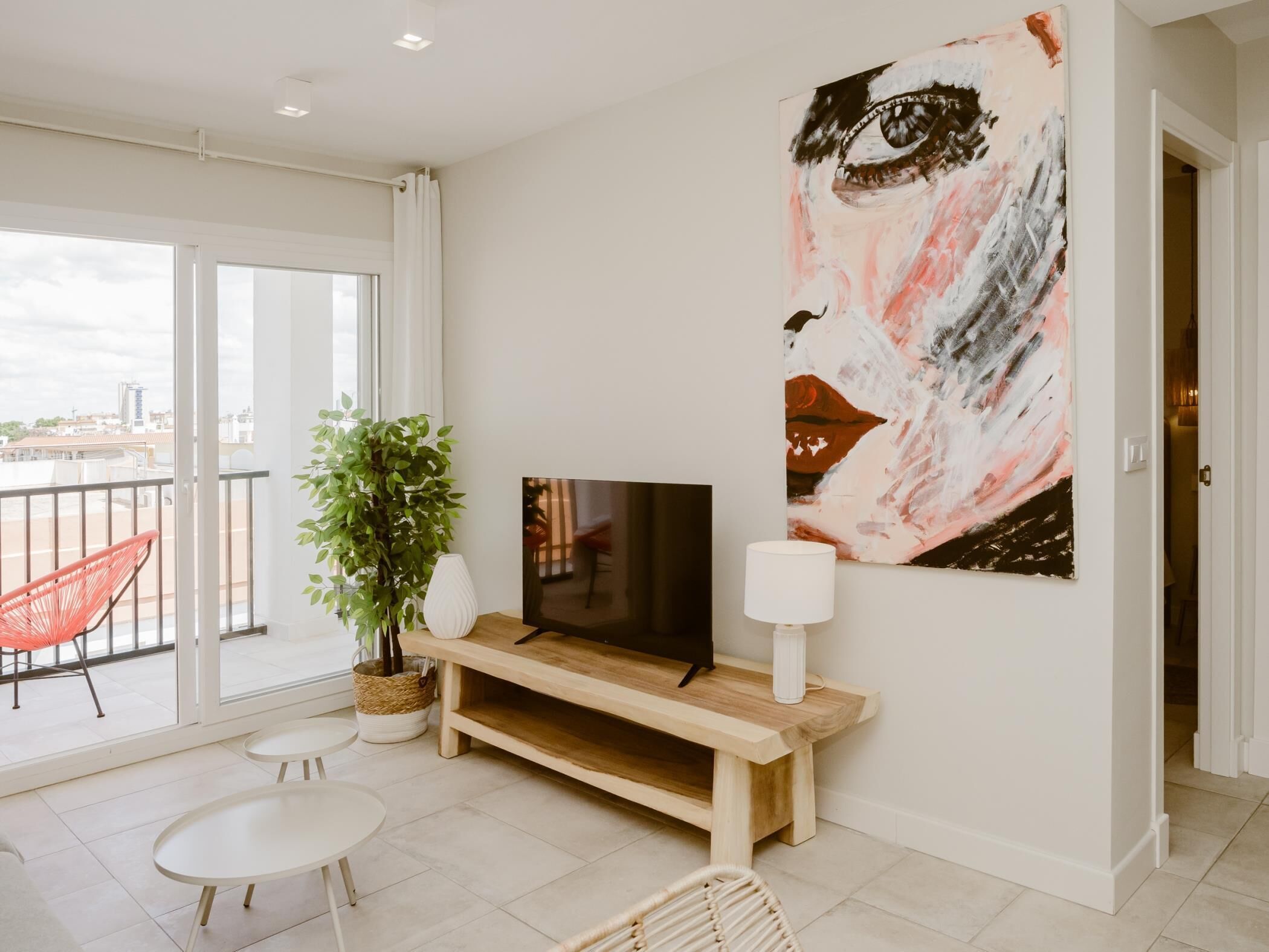A modern living room with a large window, a TV, a plant, and a painting on the wall.