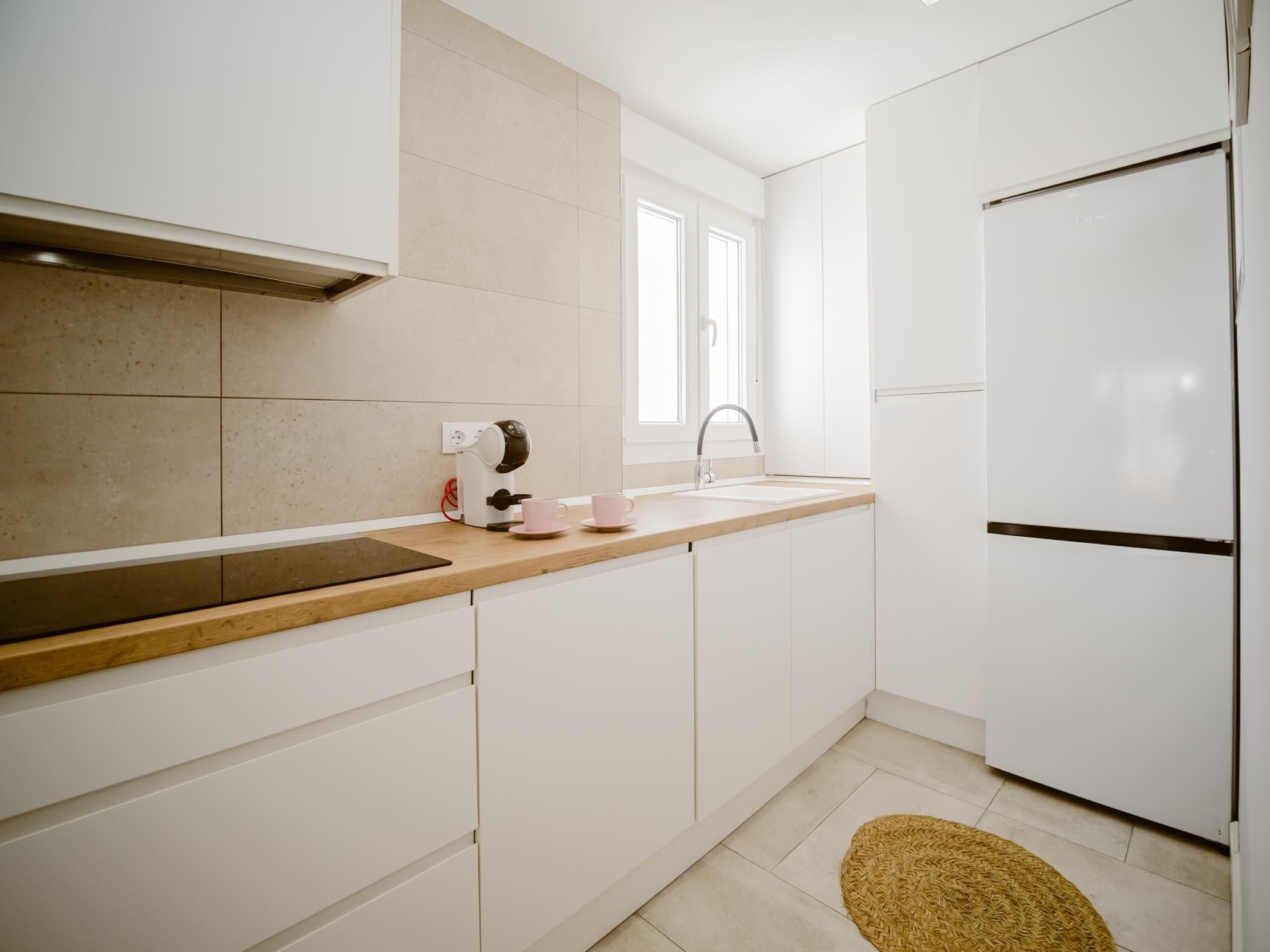 Una cocina moderna con armarios blancos, encimera de madera, horno integrado y un fregadero.