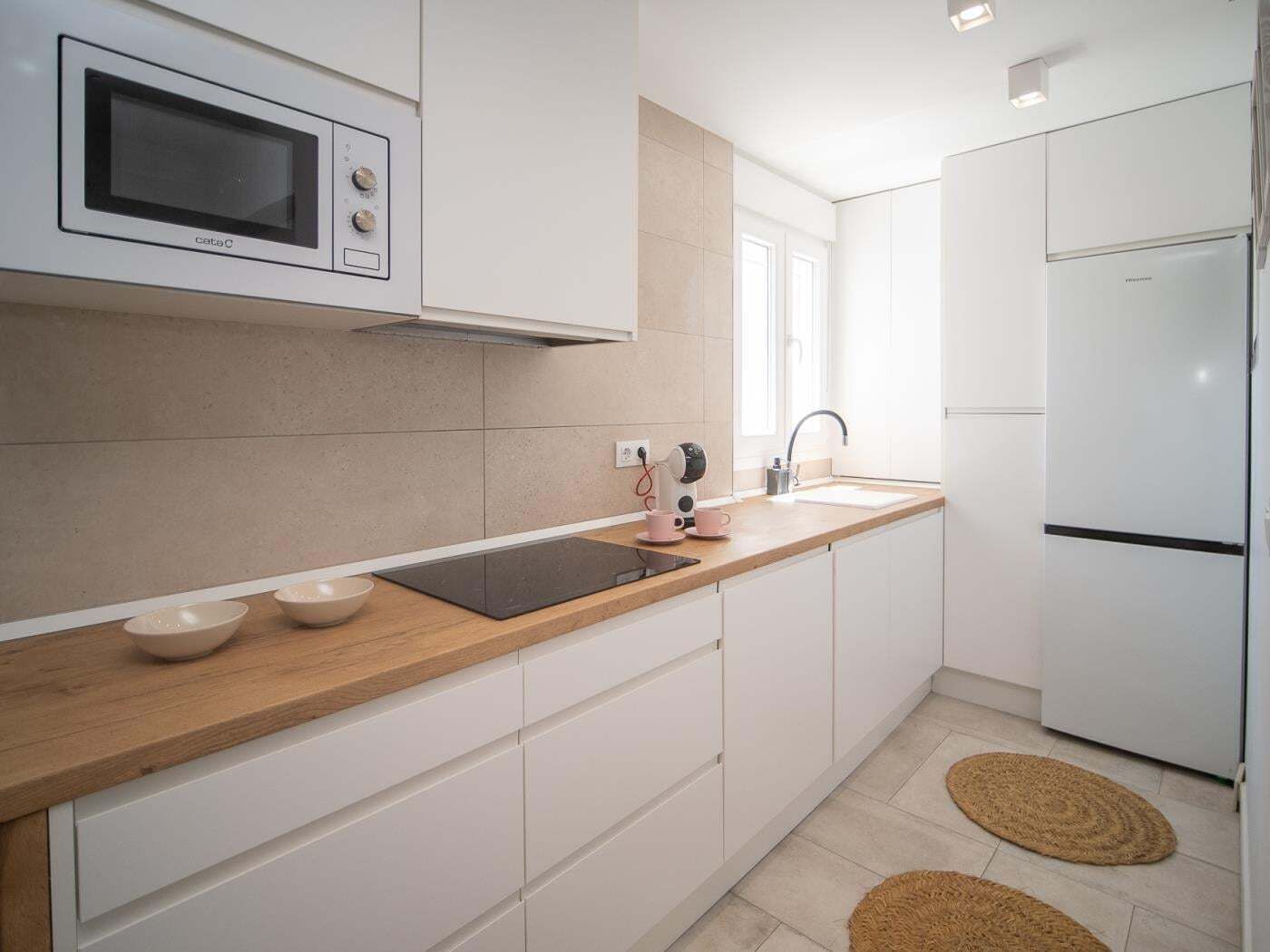 A modern kitchen with white cabinets, a built-in microwave, a stainless steel refrigerator, and a wooden countertop.