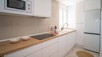 A modern kitchen with white cabinets, a built-in microwave, a stainless steel refrigerator, and a wooden countertop.