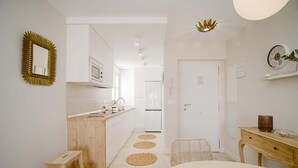 A modern kitchen with white cabinets, a wooden countertop, and a white refrigerator. There is a wooden stool and a woven chair in the foreground.