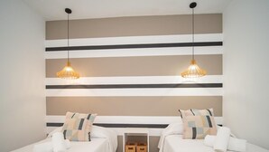 A hotel room with two beds, a white wall with horizontal stripes, two pendant lights, and a small white shelf with baskets.