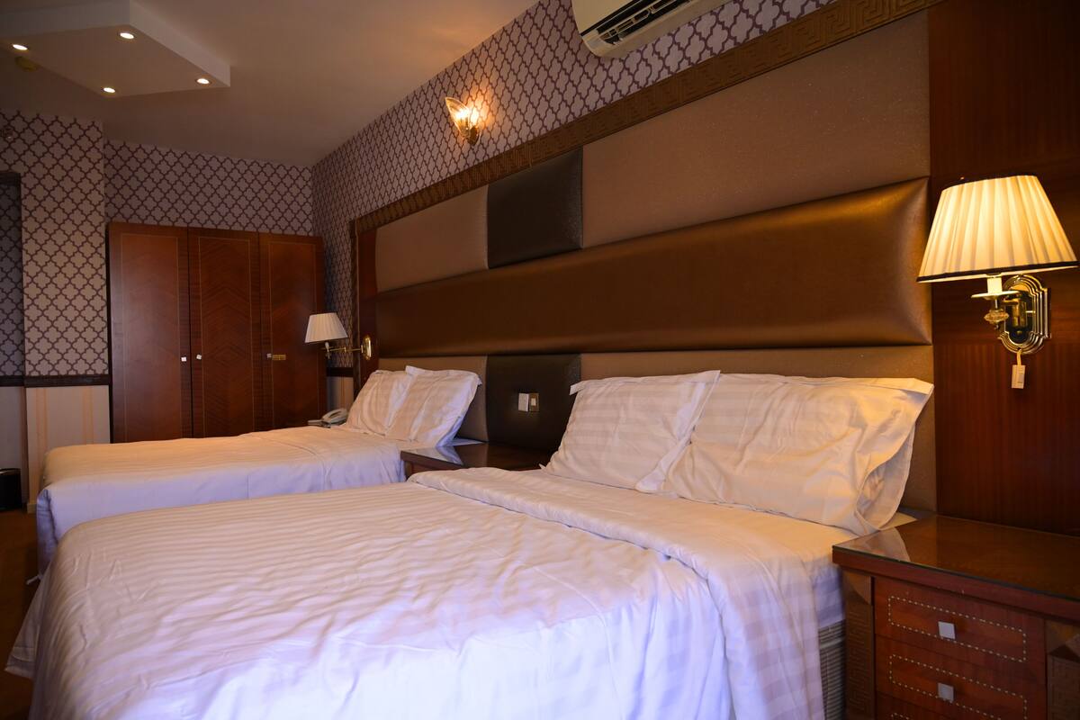Ein Hotelzimmer mit zwei Betten, einem Holz-Kopfteil, einer Nachttischlampe und einer Wand mit Muster.