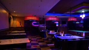 A dimly lit bar area with checkered flooring, tables, and chairs. - ABJAD CROWN HOTEL (Dubai)