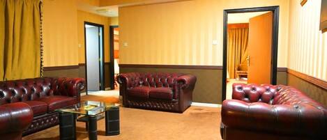A hotel room with a red leather sofa set, a glass coffee table, and a carpeted floor.