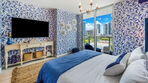 A bedroom with a city view, a large bed, a TV, and a console table with baskets. - Designer's Dream! 2 Bedroom Condo with Bay Views (Miami)