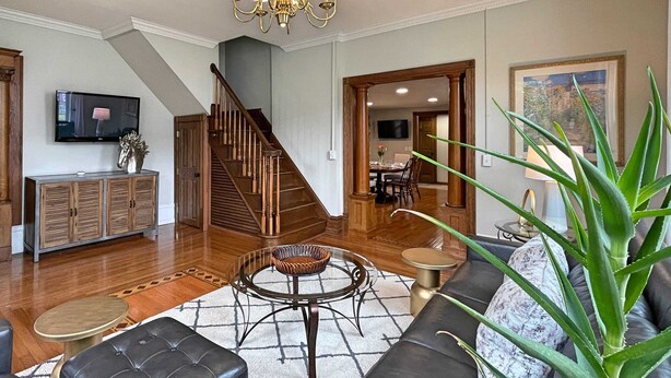 A spacious living room with a wooden staircase, a television, a dining area, and a large plant.