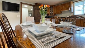 A dining table set with white plates, bowls, and cutlery, accompanied by striped placemats and a vase of flowers.