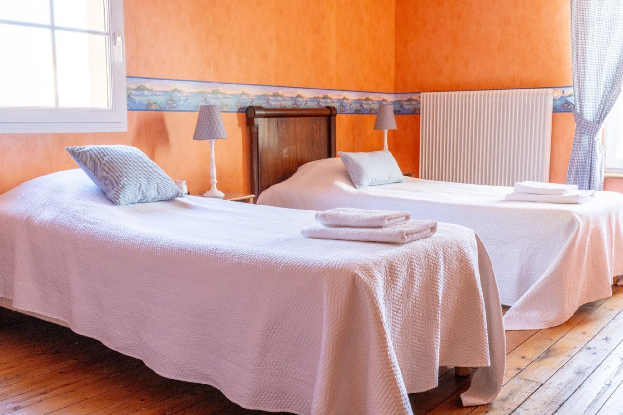 A hotel room with two beds, a wooden floor, a window, and a radiator.