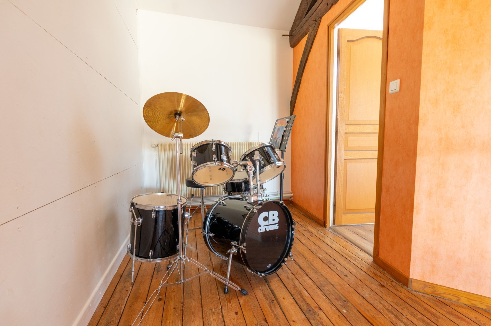 A drum set in a room with wooden flooring and a radiator in the background.