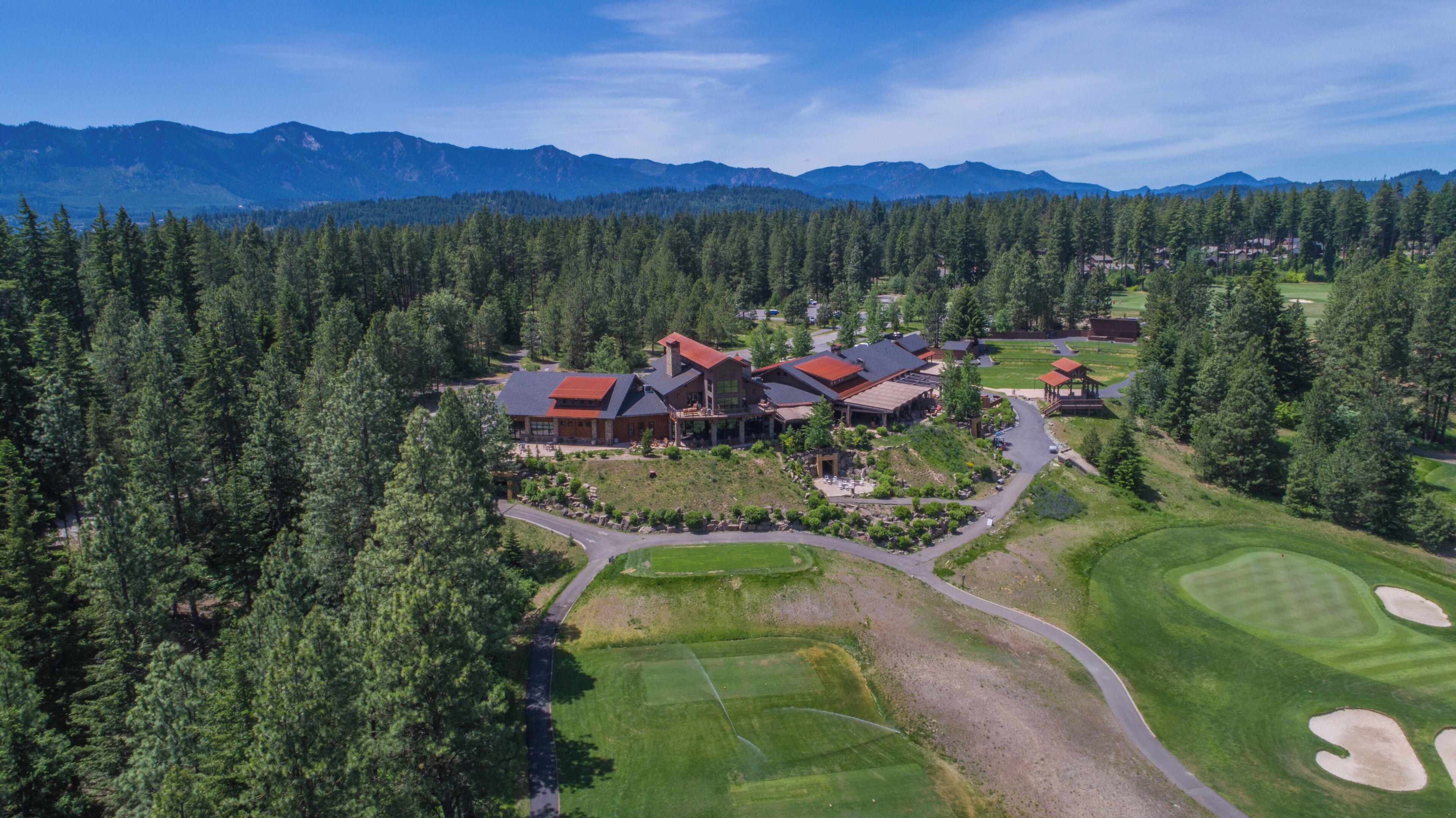 An aerial view of a lodge with multiple buildings, surrounded by dense forest and mountains.