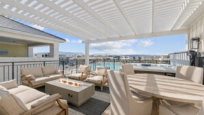 Eine Dachterrasse mit Sitzgelegenheiten im Freien, einer Feuerstelle und Blick auf ein Schwimmbad und Berge.