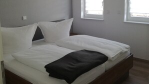 Un dormitorio con cama, paredes blancas, suelo de madera y una lámpara en el techo.