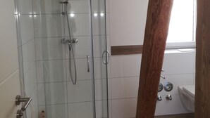 Una ducha envuelta en vidrio con cabezal de ducha manual y llave empotrada en la pared.