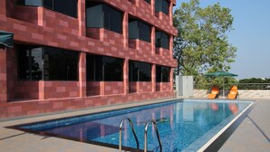 A swimming pool with metal railings, a tiled deck, and a building with a brick facade. - THE SOUTH PARK (Thiruvananthapuram)