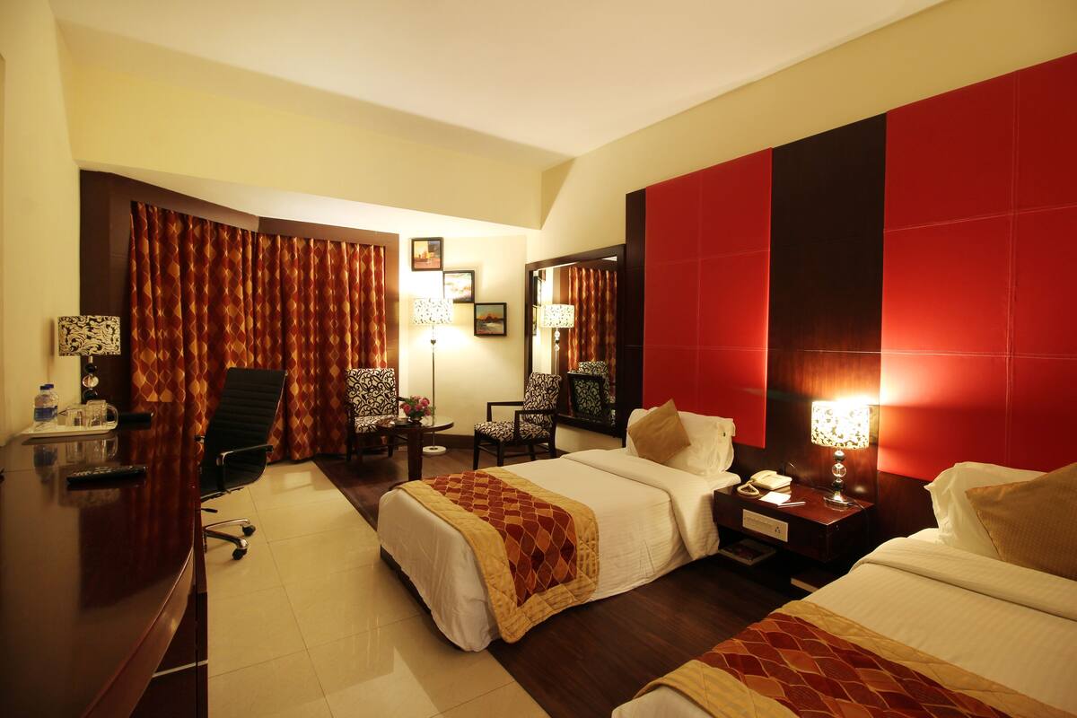 Habitación de hotel con dos camas, un escritorio, una silla y una mesita de noche con lámpara.